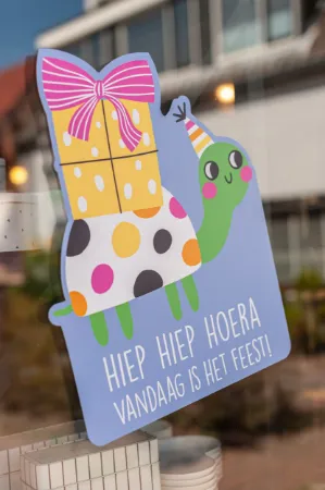 Sfeerbeeld raamsticker met kleurrijke felicitatie en feestschildpad voor verjaardagen of feestdagen.