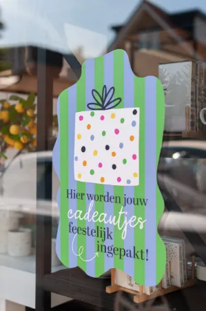 Sfeerbeeld raamsticker 'Hier worden jouw cadeautjes feestelijk ingepakt' op een raam in de etalage